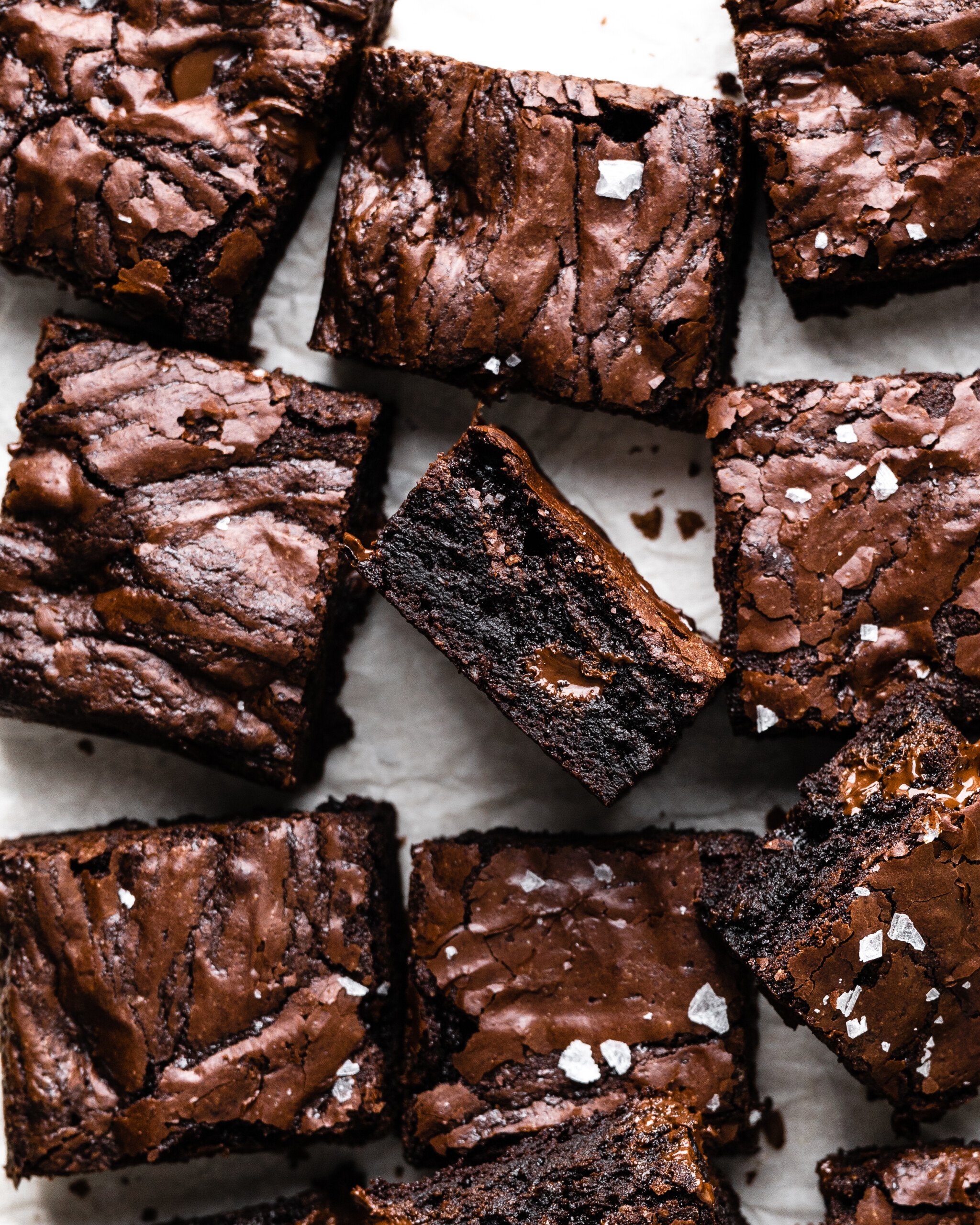 shiny sourdough brownies cut into squares topped with sea salt with one slice flipped to the side