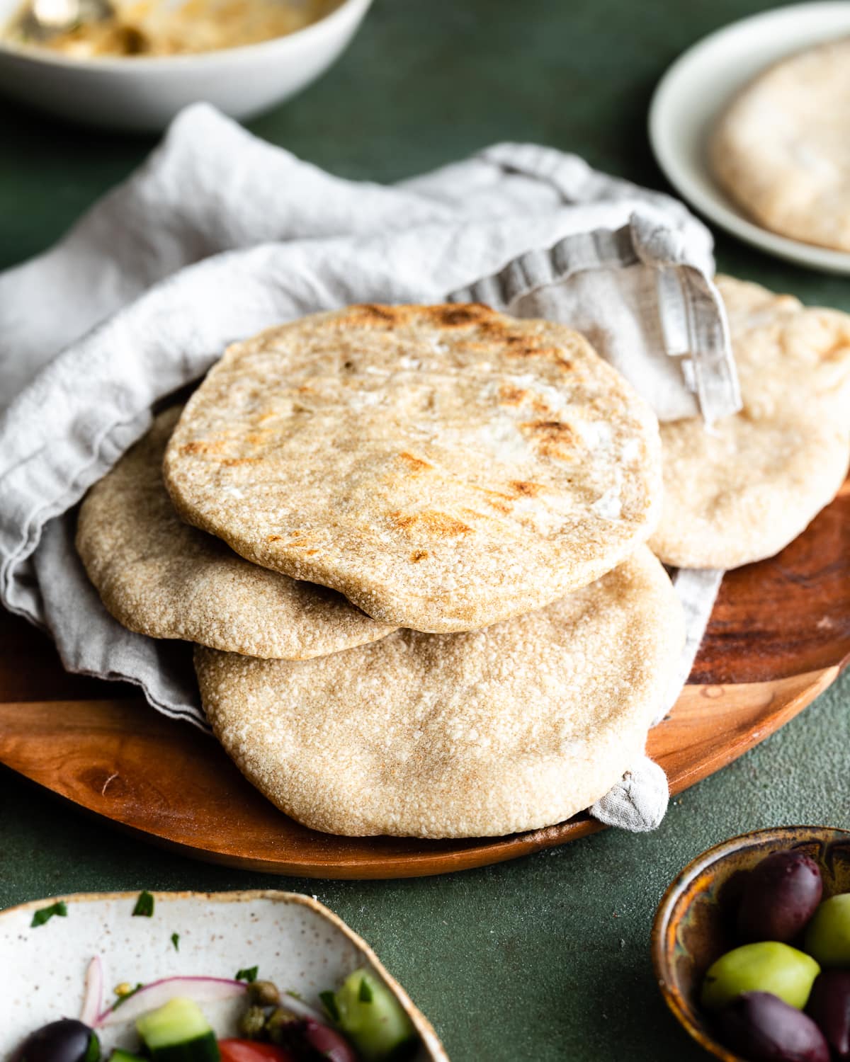 Stack of pita on a wooden plate wrapped in a tea towel