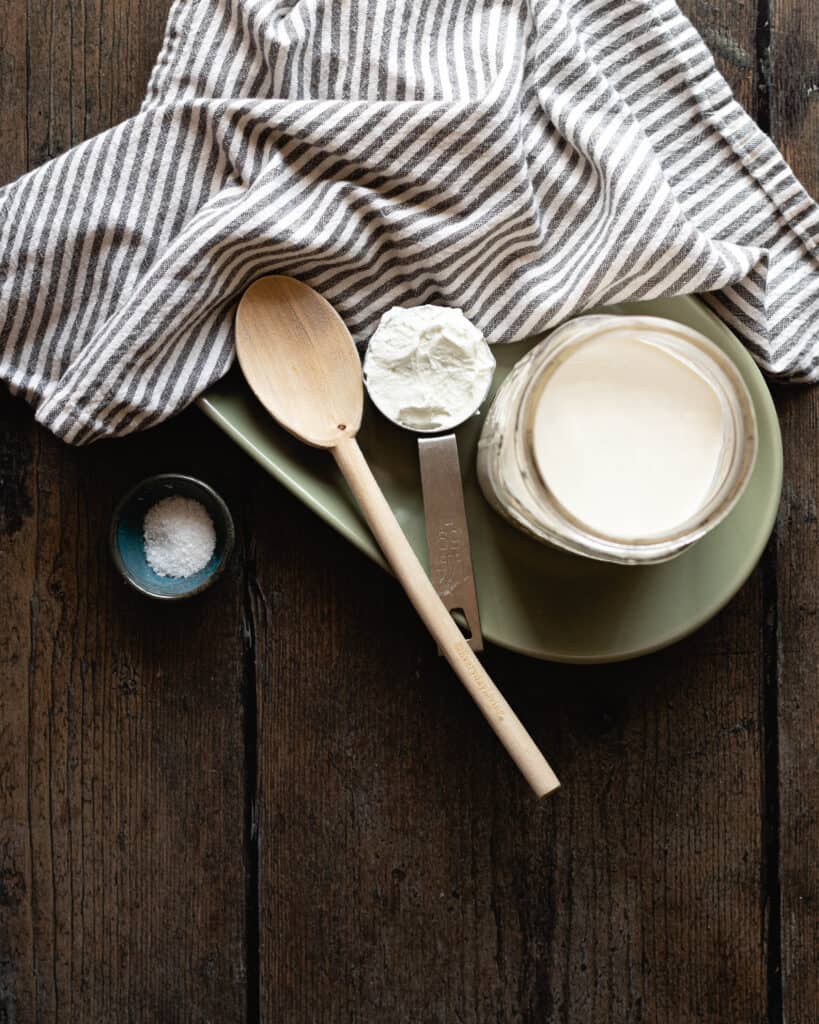 salt, wooden spoon, yogurt in a measuring cup and heavy cream in a jar for cultured butter recipe