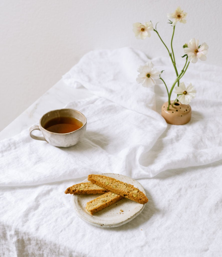 stack of sourdough biscotti on a table with a tablecloth, tea and a flower vase.