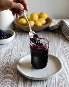 spoon scooping up blueberry preserves in a small jar