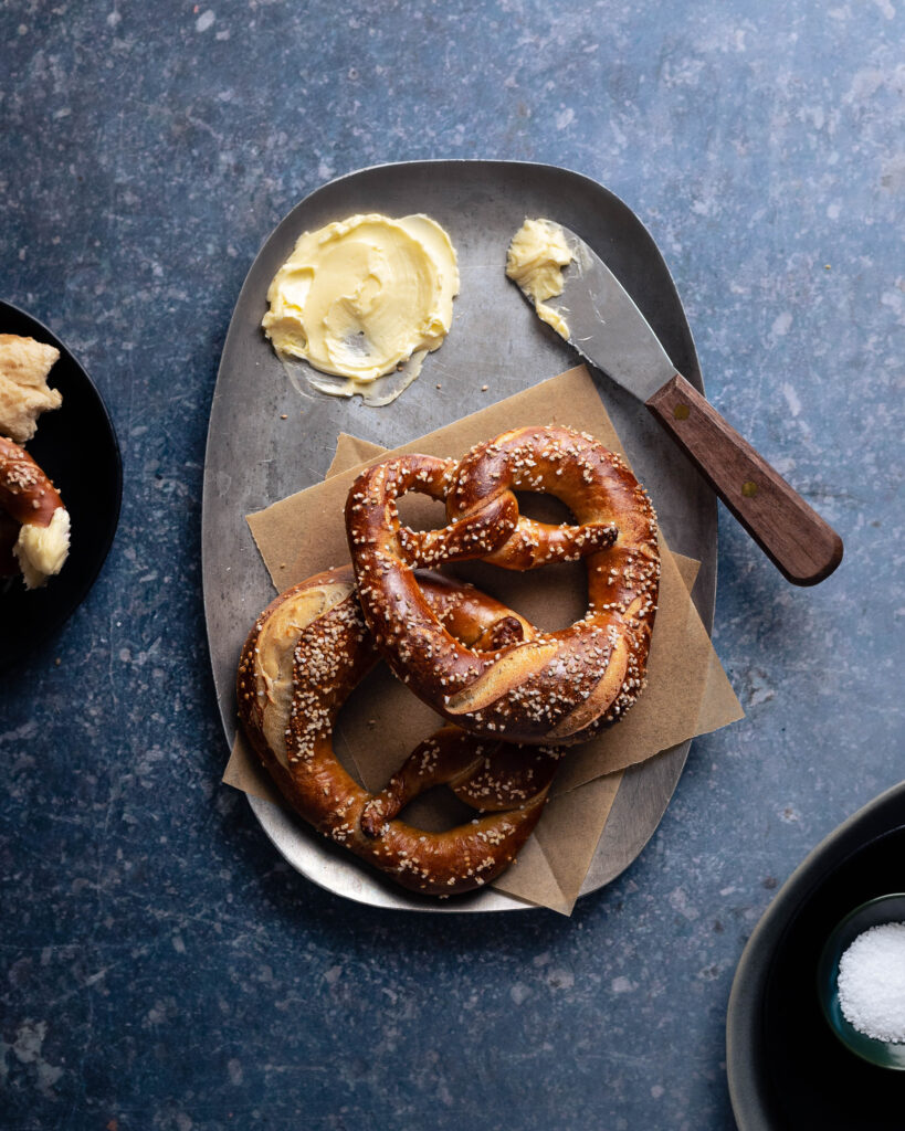 Two sourdough soft pretzels with a soft butter and a spreader 