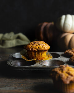 Pumpkin muffin on a muffin tin with the liner peeled back.