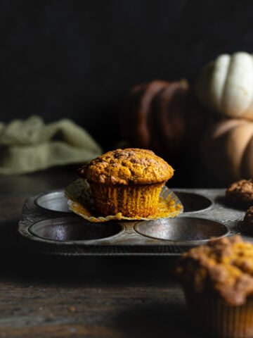 Pumpkin muffin on a muffin tin with the liner peeled back.