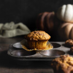Pumpkin muffins with wrapper peeled back on a muffin tin with pumpkins in the background