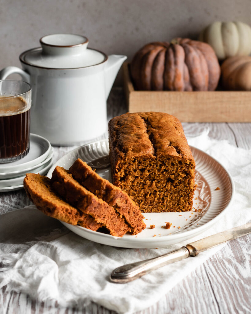 Sliced loaf of sourdough pumpkin bread on serving platter with pumpkins in the background