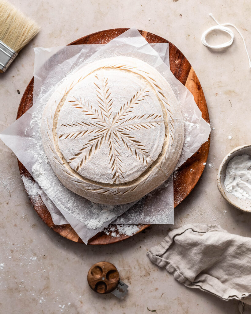 Dough scored with a snowflake pattern on a parchment on a wooden platter 