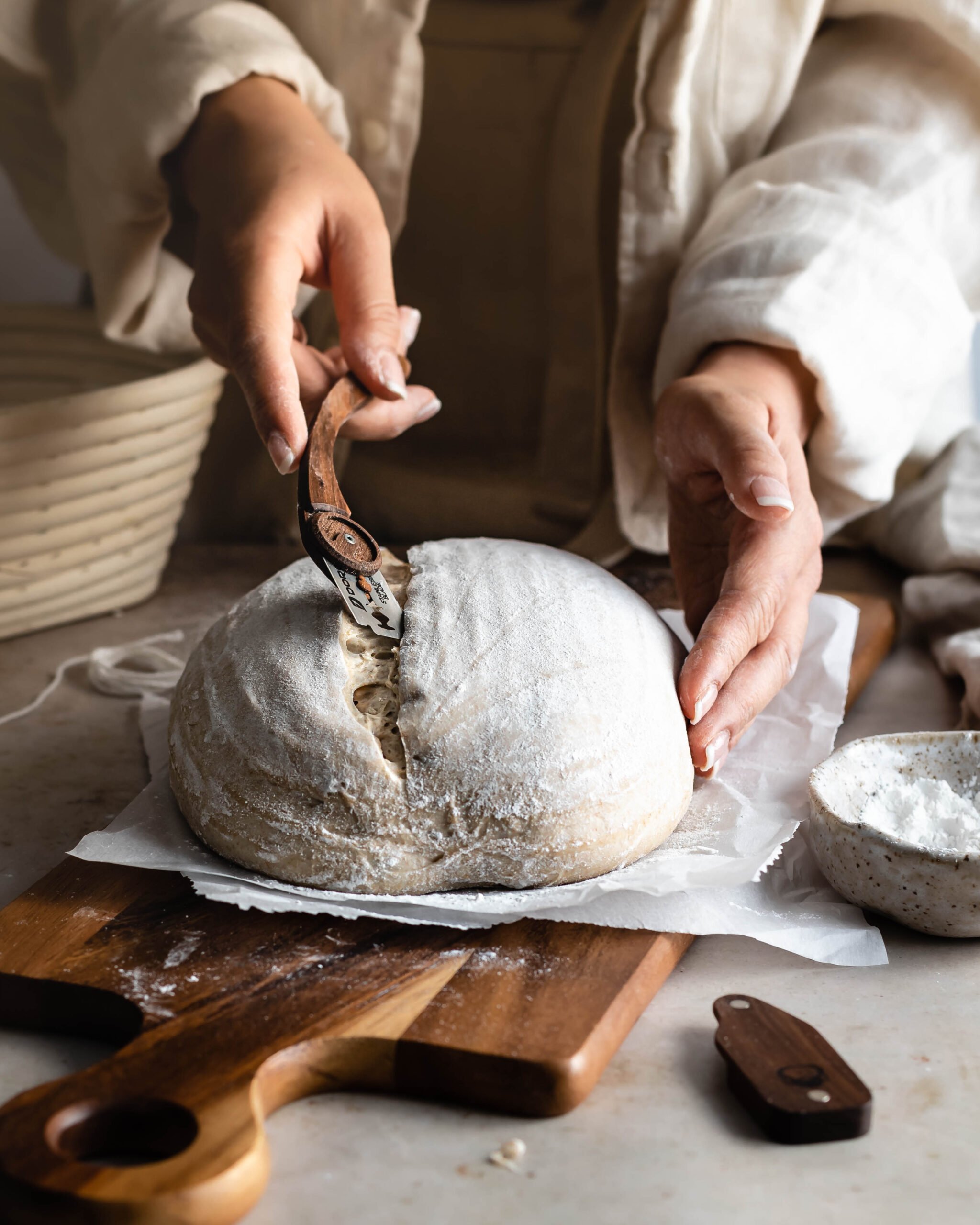 Hand holding a bread lame scoring dough on a cutting board