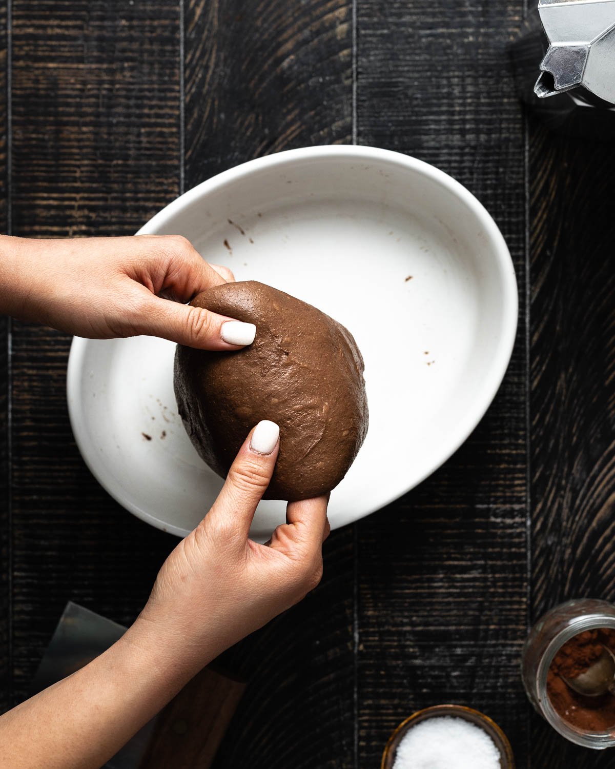 hands lifting chocolate dough in a white platter