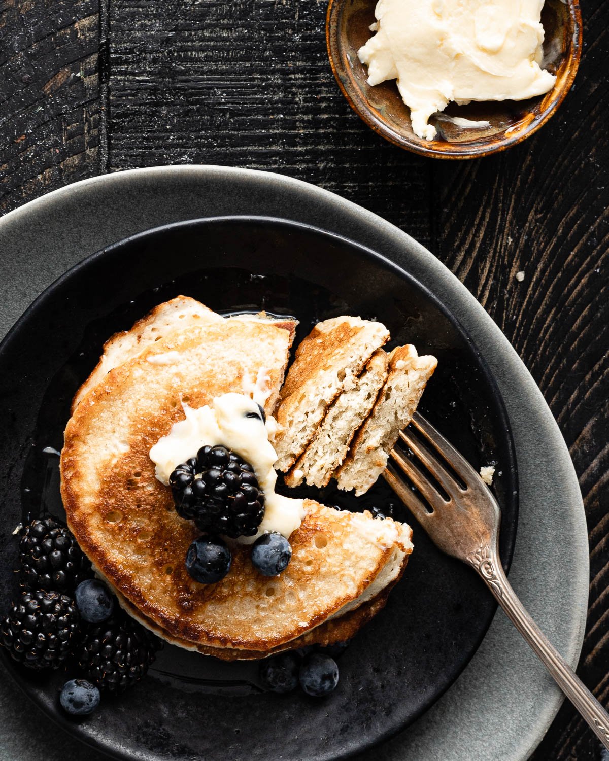 Pancakes on a plate with a section cut off and a fork skewering layers of pancakes. 