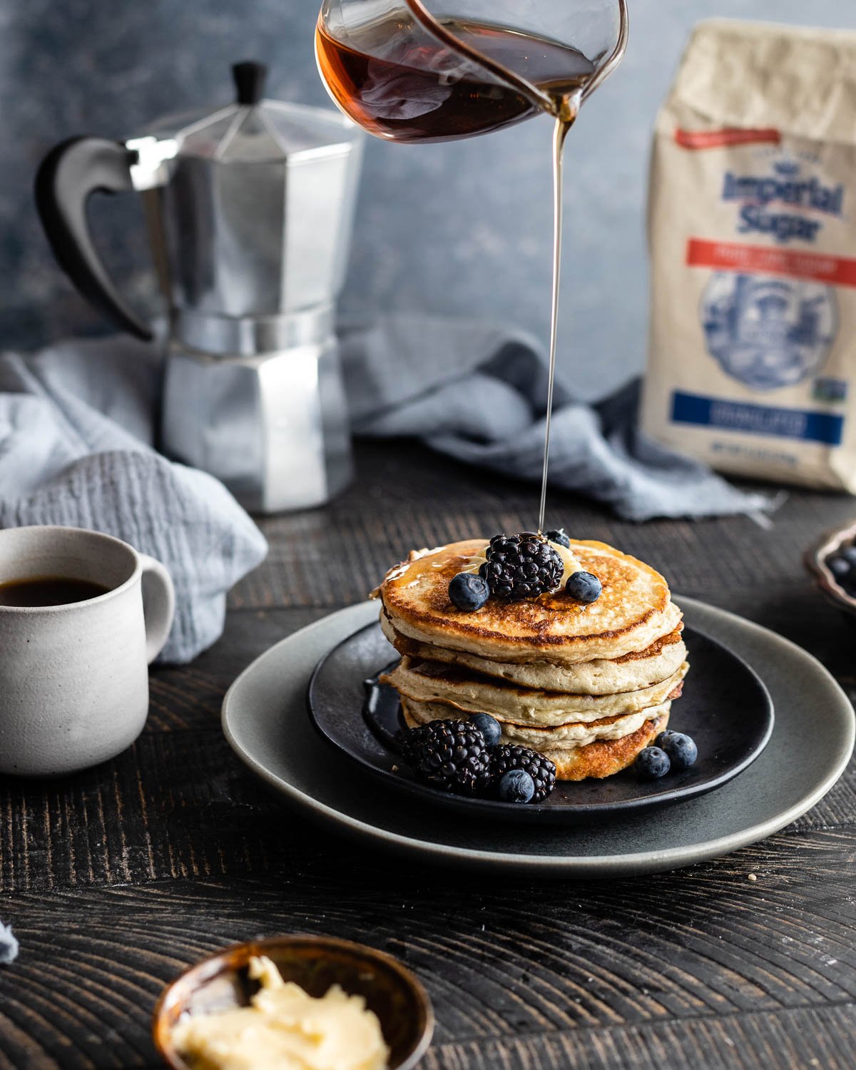 Stack of pancakes on a plate with maple syrup being drizzled on top. 