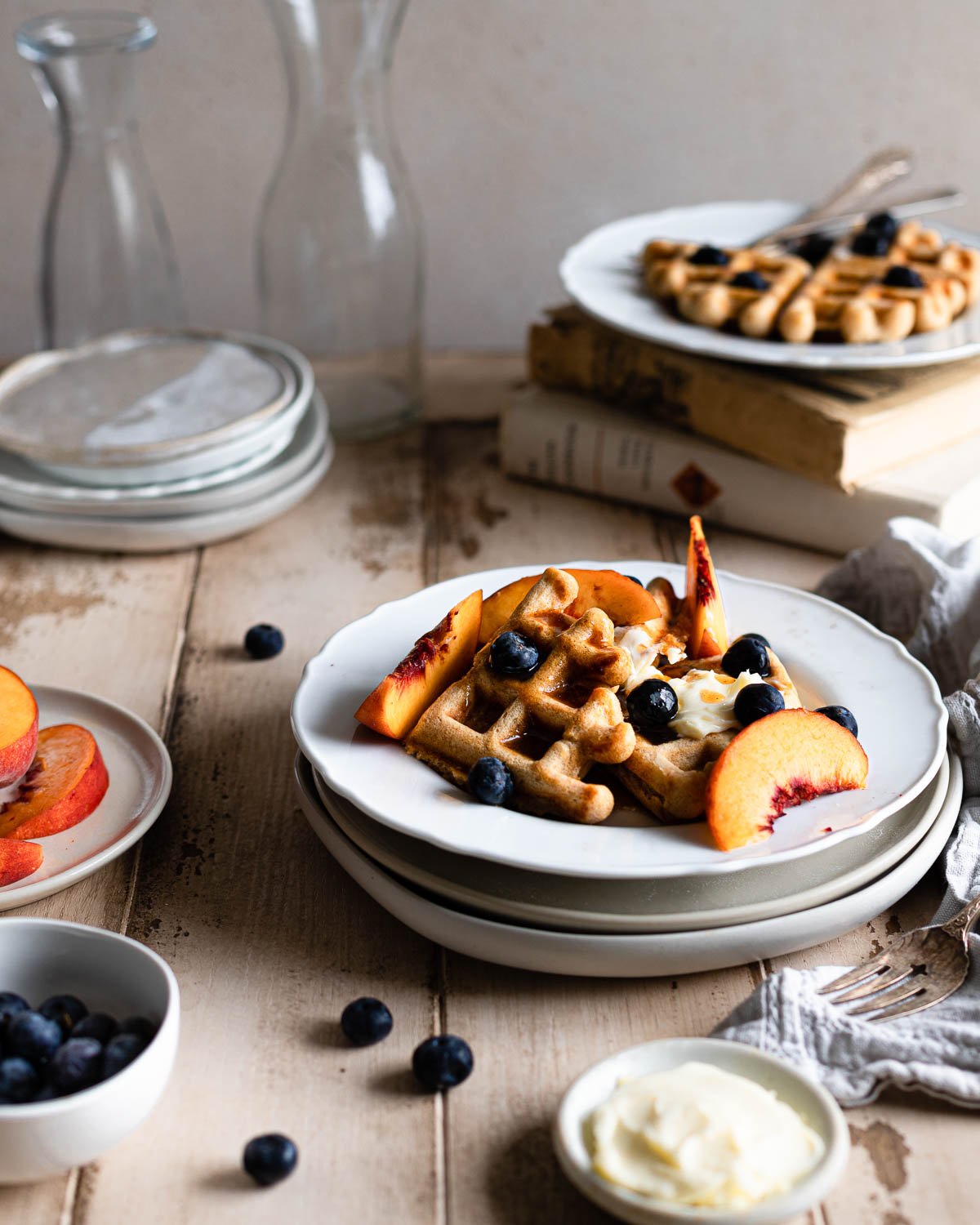 Cut up waffle on a stack of plates with blueberries and peaches. 