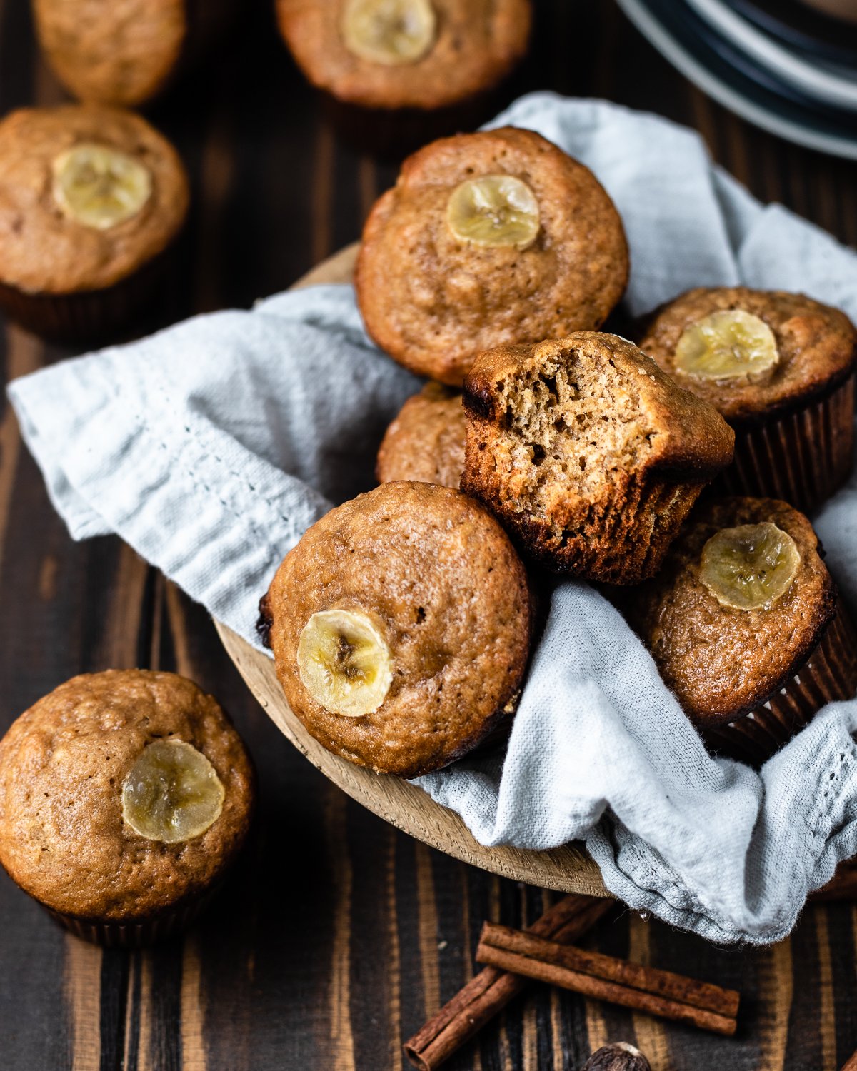 muffin with bite taken out on top of a pile of banana muffins inside a wood bowl