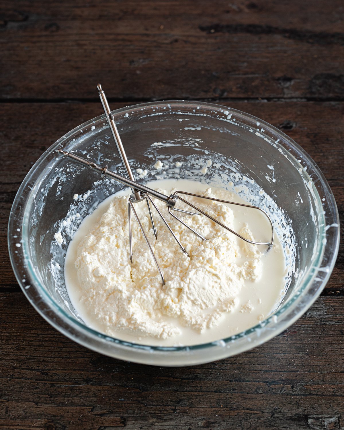 whipped cream with curds and whey separated inside a glass bowl with wire beaters
