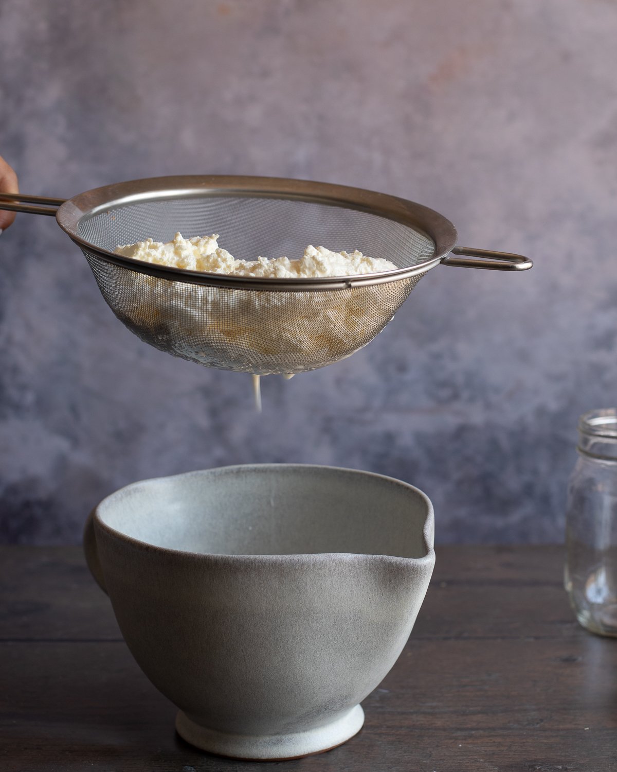 curds strained in wire strainer over a ceramic measuring bowl