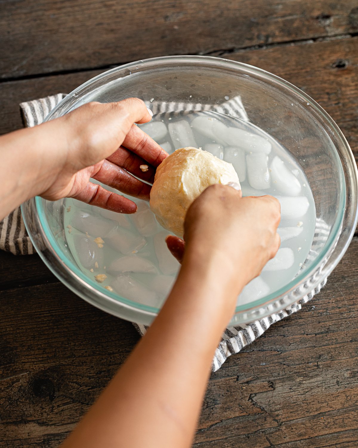 hands holding a ball of butter over a glass bowl of ice water