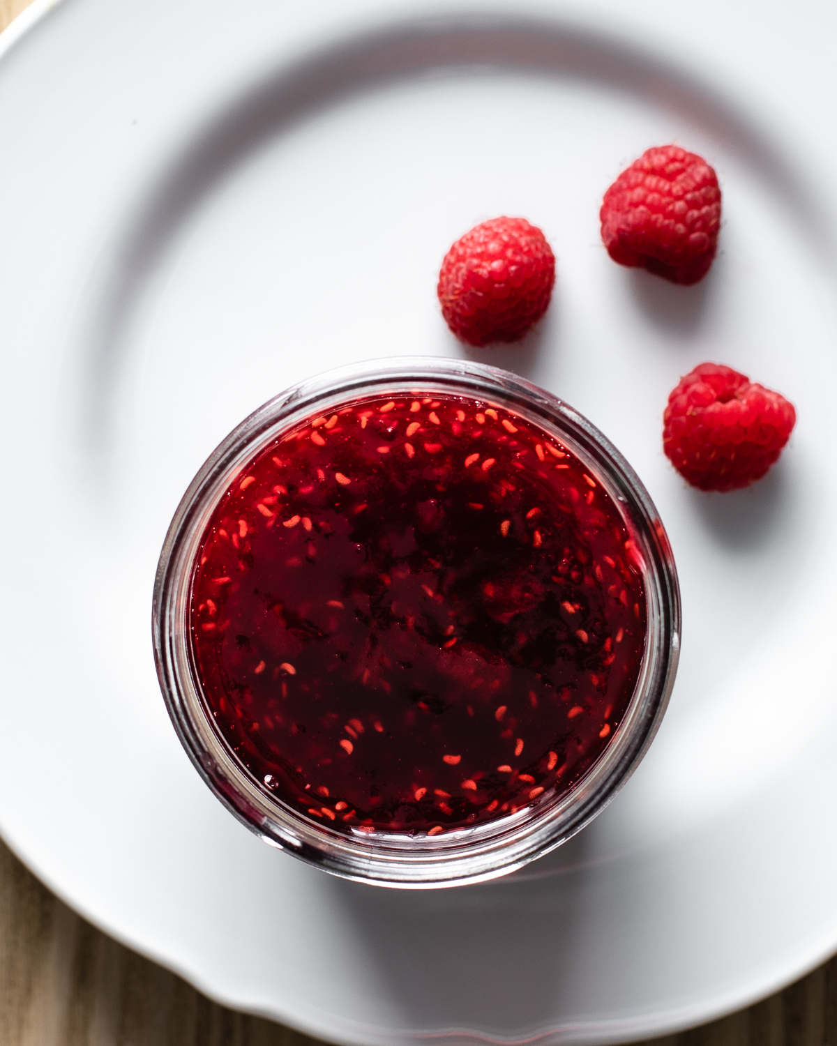 raspberry preserves in a glass jar on a white plate. 
