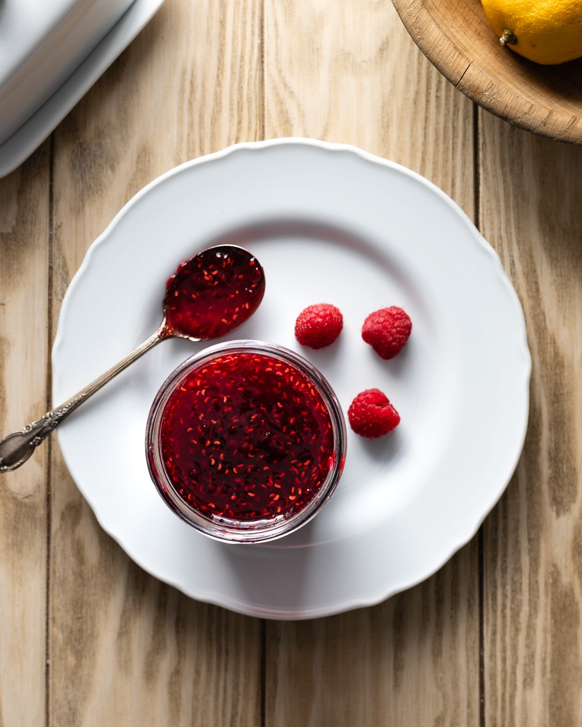 raspberry preserves in a jar on a plate with raspberries.
