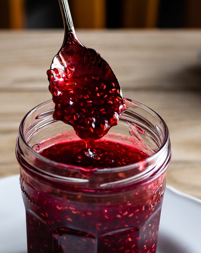 spoon scooping raspberry preserves from a jar. 