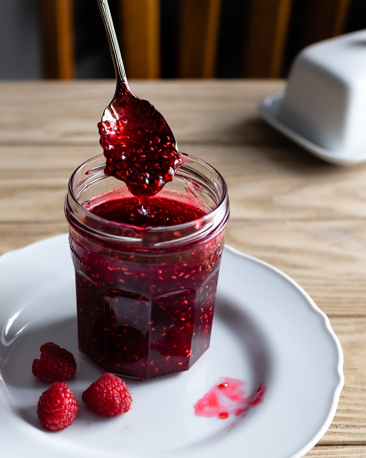 spoon scooping chunky raspberry preserves in a jar on a plate.