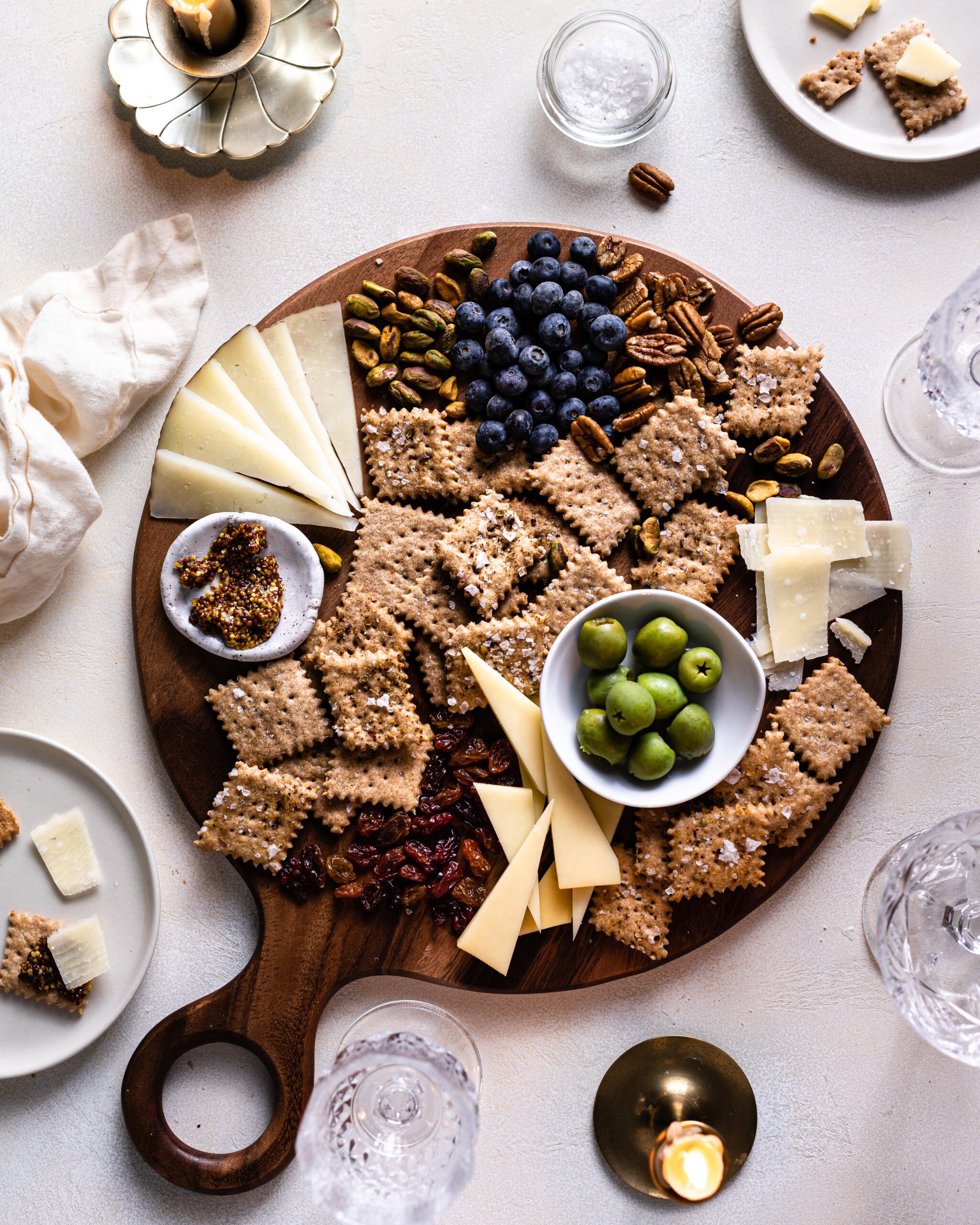 sourdough crackers in the center of a cheese board with cheeses, raisins, olives and mustard