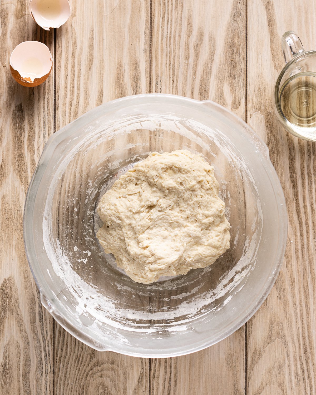 dough in a large mixing bowl with egg shells and vegetable oil in small gravy boat