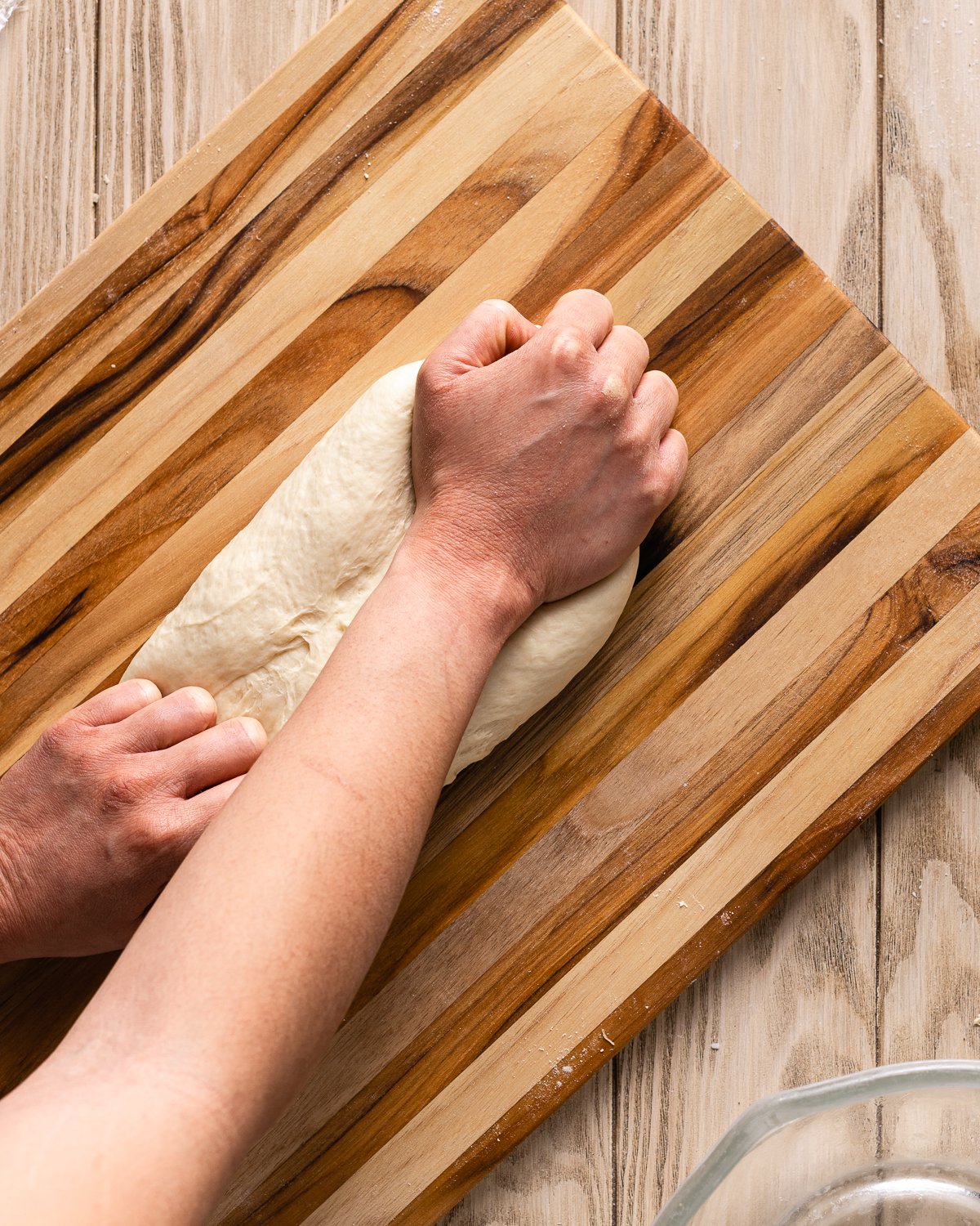 hands kneading dough on a wood cutting board