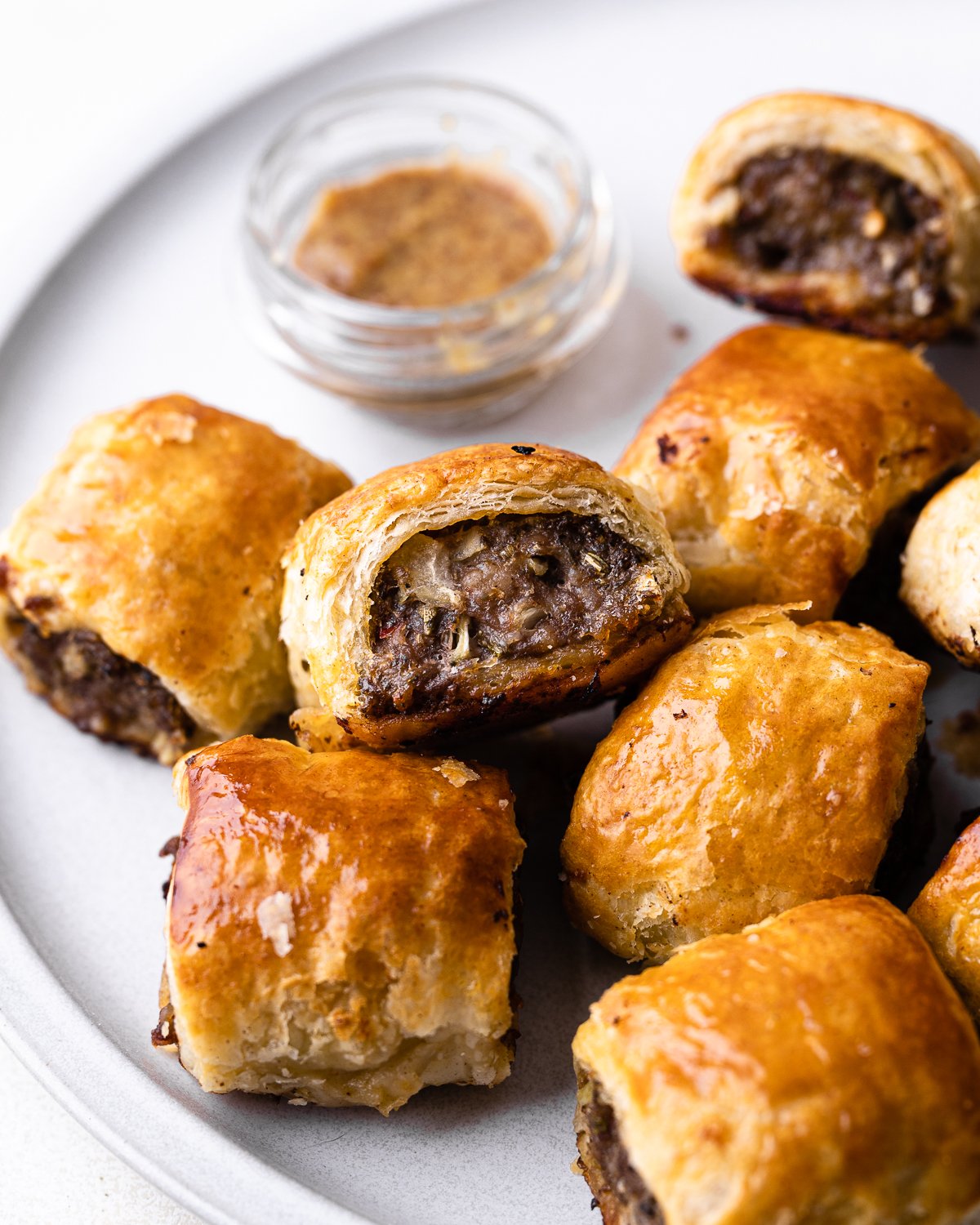 Pile of sausage rolls on a plate with mustard dipping sauce. 