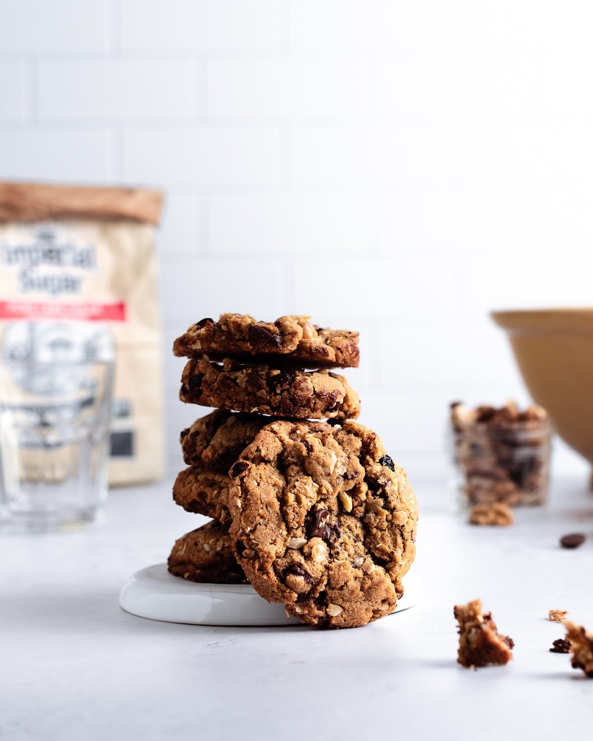 stack of oatmeal cookies on a plate with a bag of sugar and yellow mixing bowl in the background