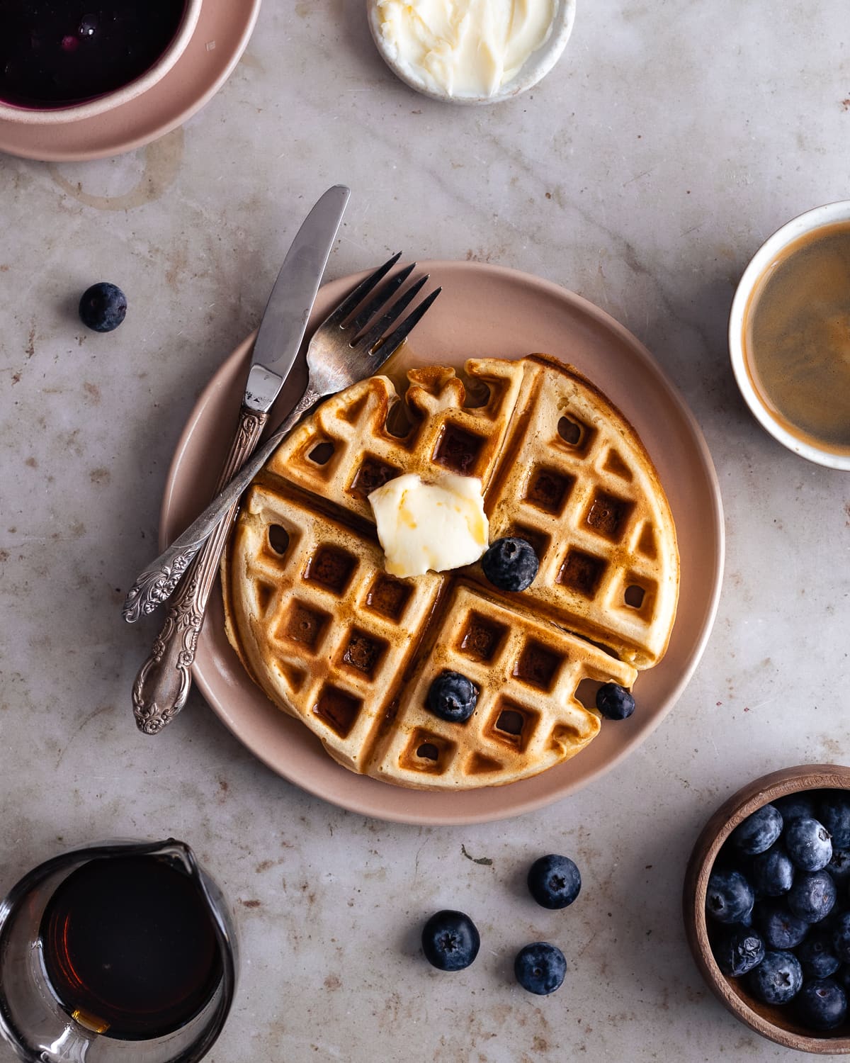 Waffle with a pat of butter on top, maple syrup and blueberries. 