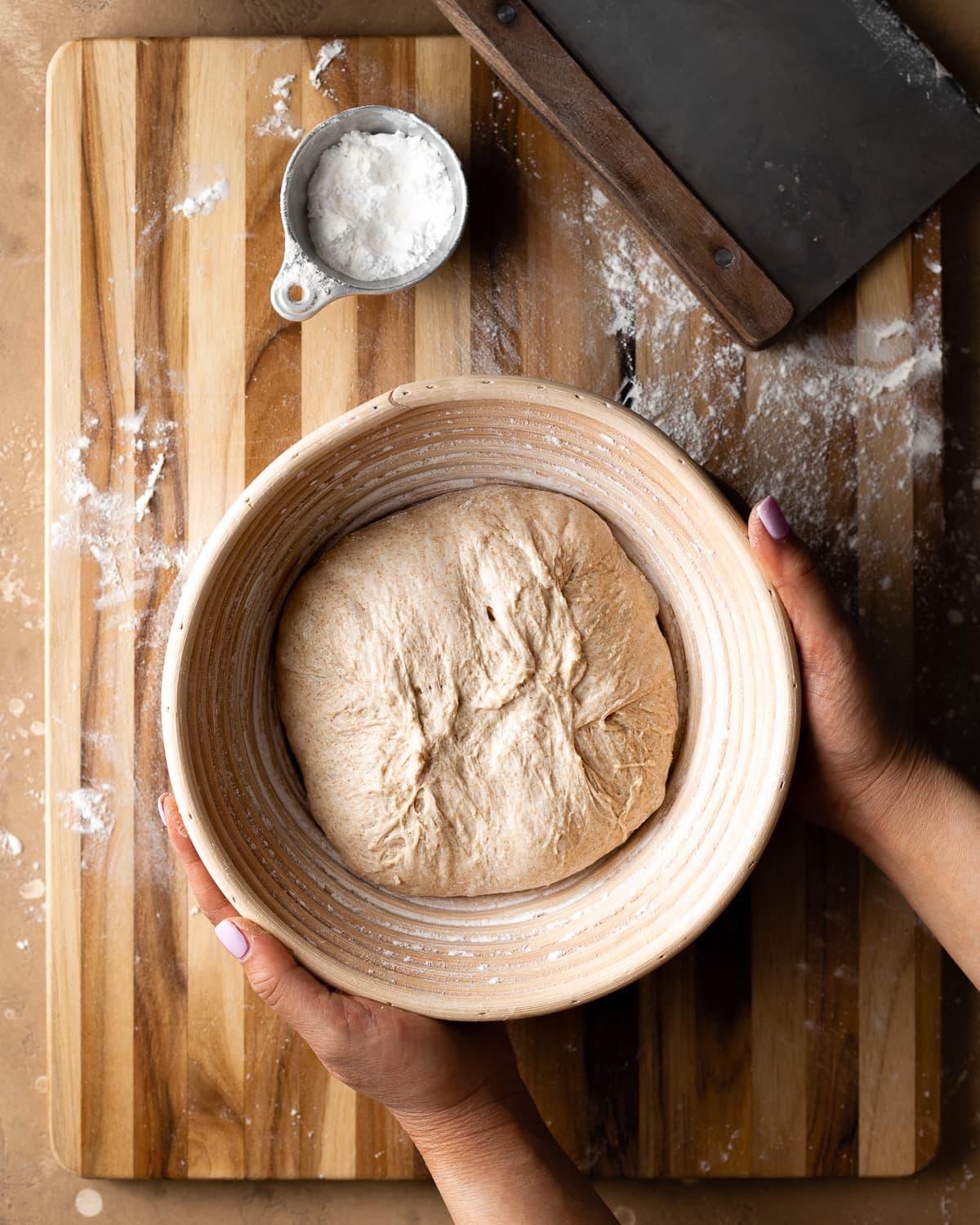 hands holding shaped sourdough dough inside a round banneton