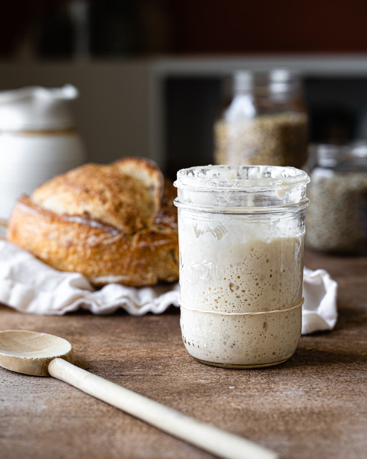 a jar of bubbly sourdough starter with a loaf of bread in the background