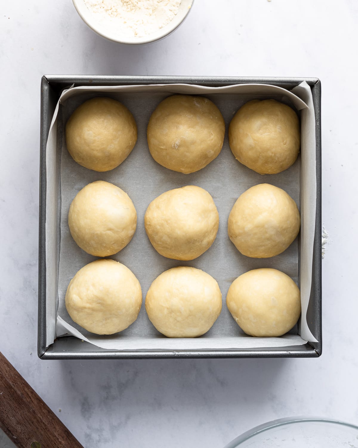 unrisen dough balls in a square baking pan lined with parchment. 