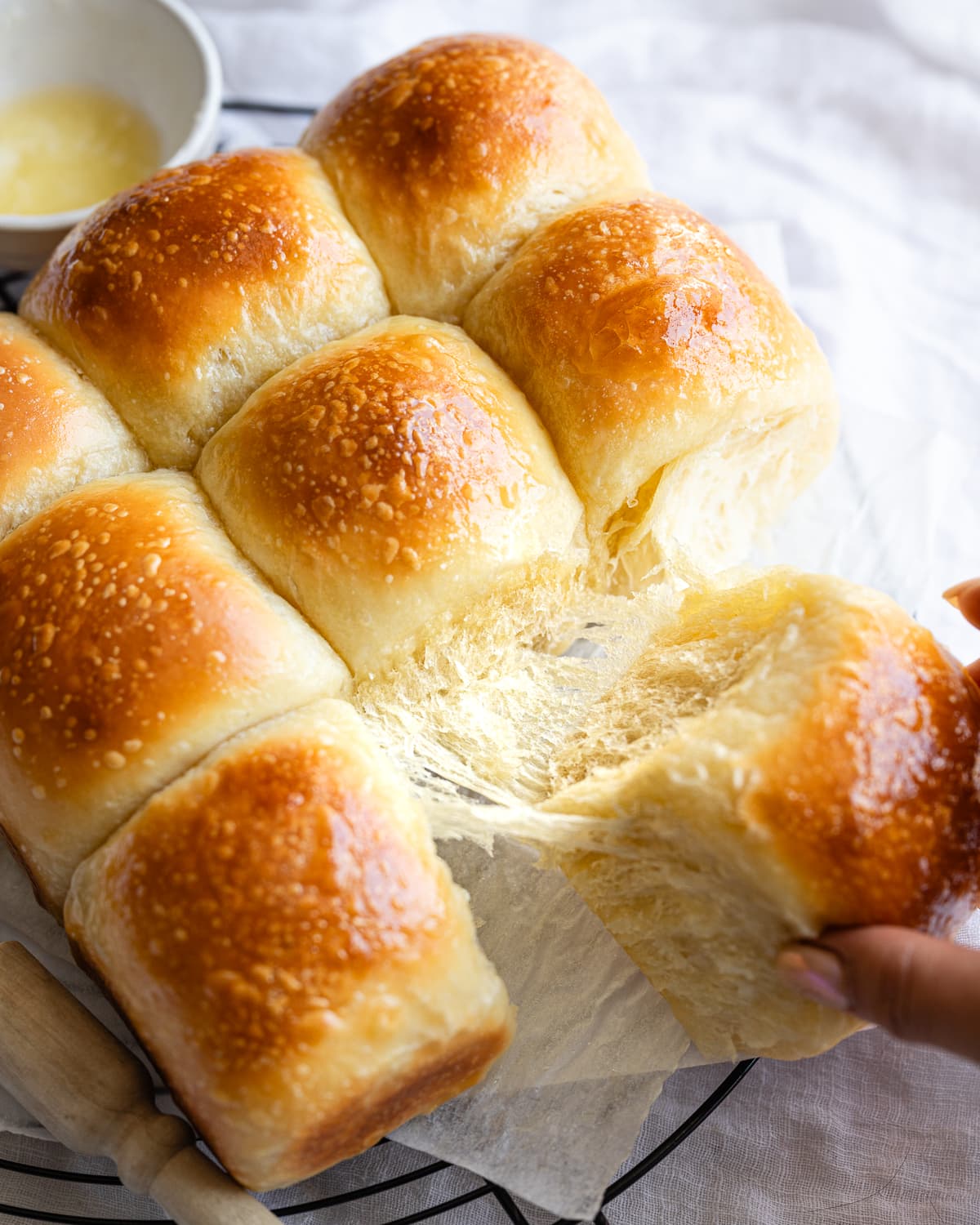 hand pulling off a bread roll from a batch of baked rolls. 