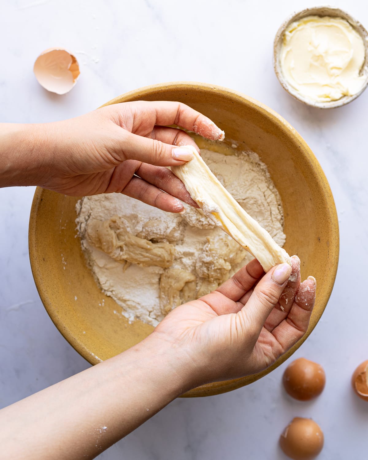 hands tearing stiff starter over bowl of dough. 