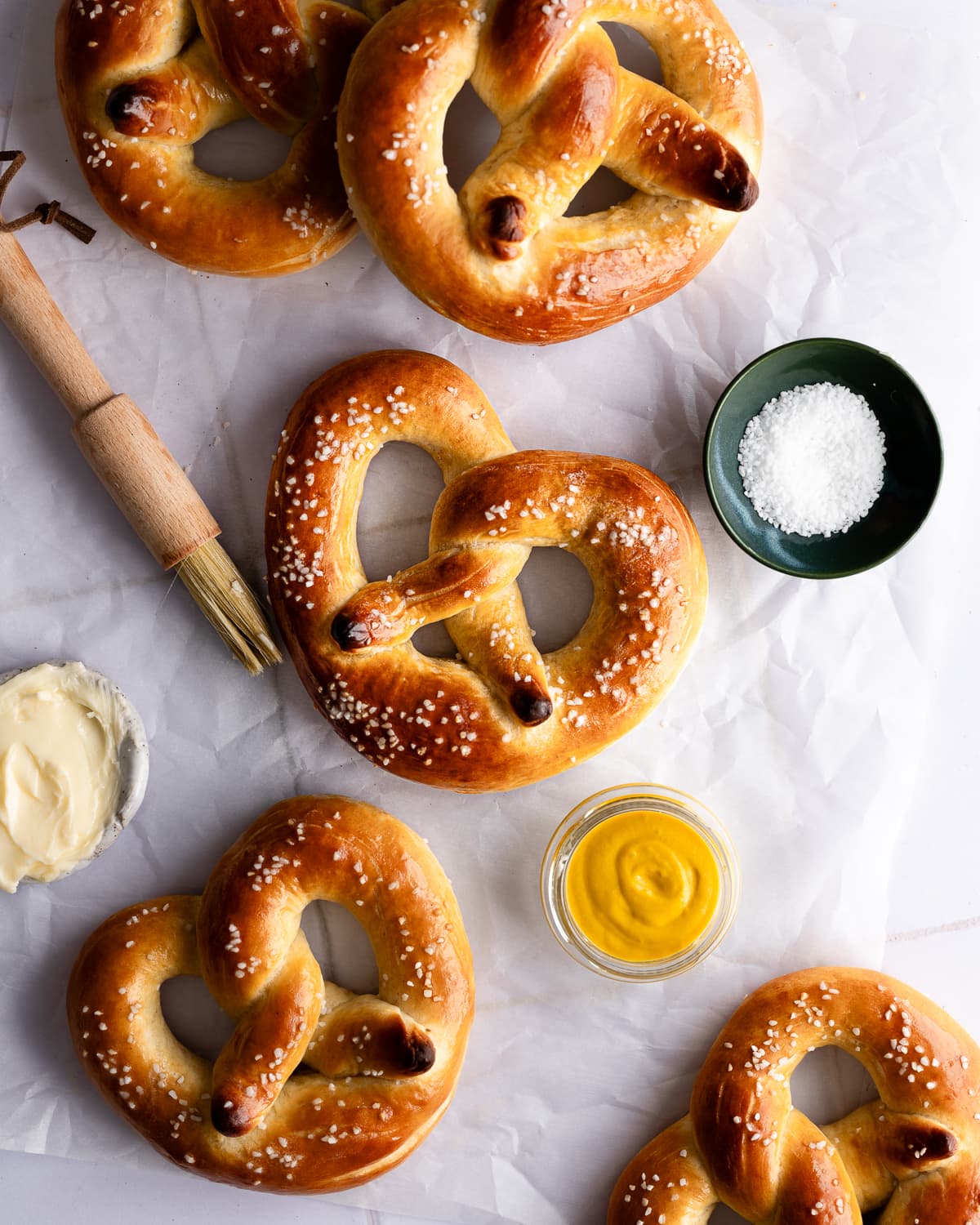 Soft pretzels on a piece of parchment paper with mustard and butter. 