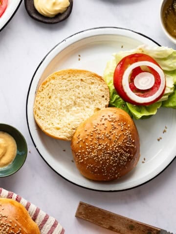 Split hamburger bun on a plate with lettuce, tomatoes and onion.