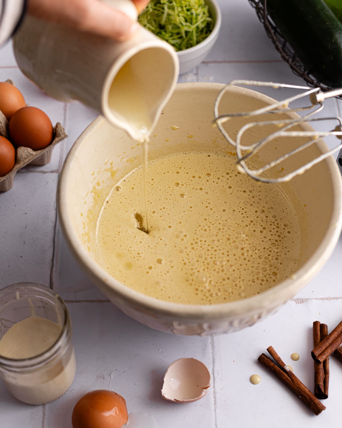 Oil streamed into zucchini bread batter in a white bowl. 