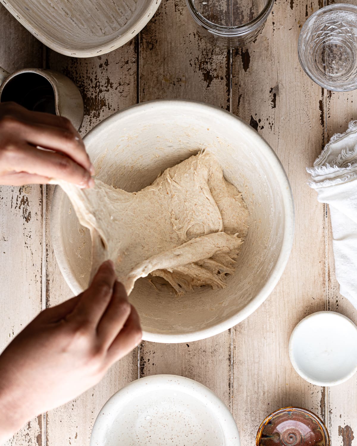 hands folding dough inside a mixing bowl. 