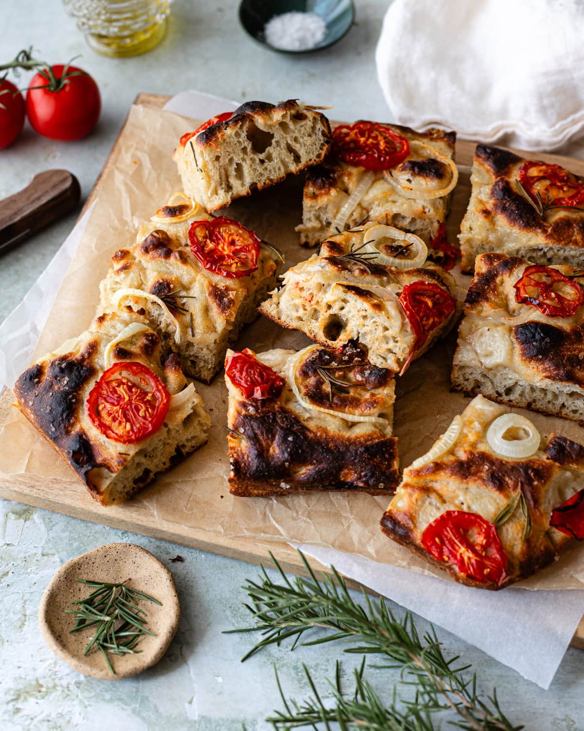A whole focaccia topped with onions and tomatoes sliced into squares on a parchment-lined cutting board.