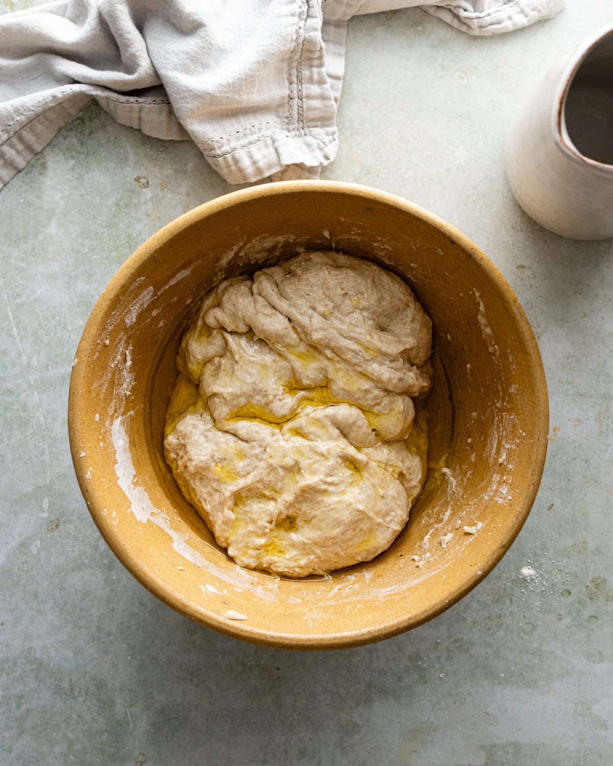Dough coated in olive oil inside a yellow mixing bowl.