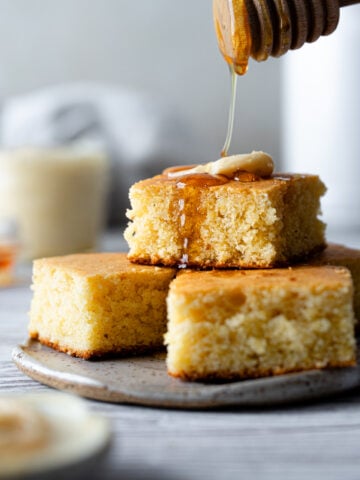 stack of cornbread with a pat of butter and honey drizzled on top