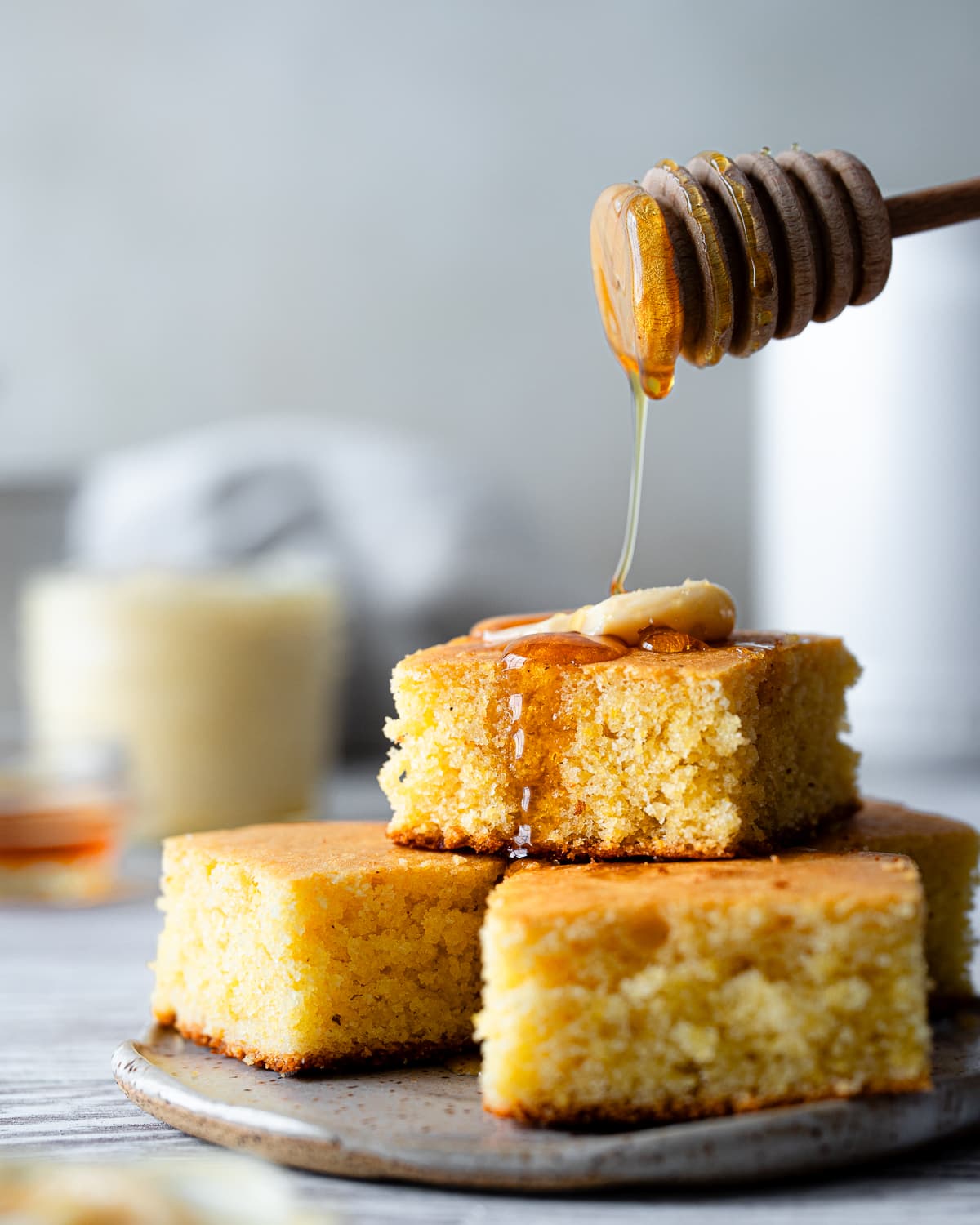 stack of cornbread on plate with pat of butter and honey being drizzled on top.