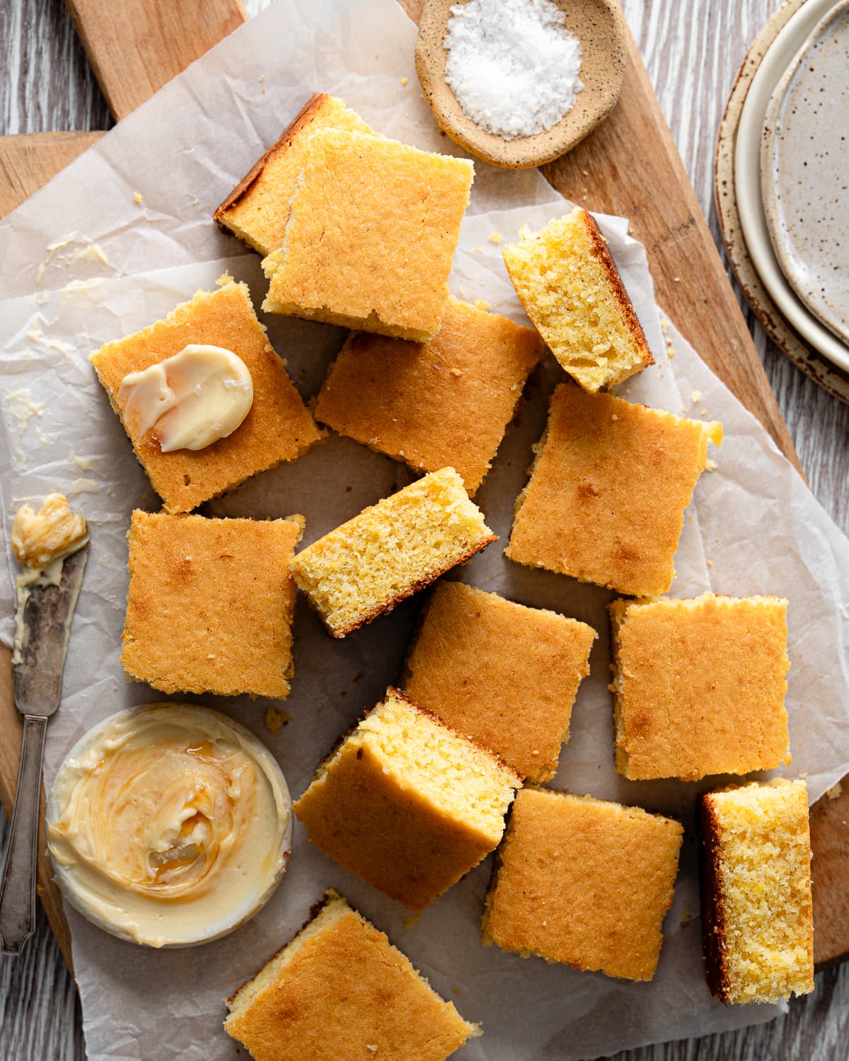 slice of cornbread on a wood cutting board with honey butter and salt. 