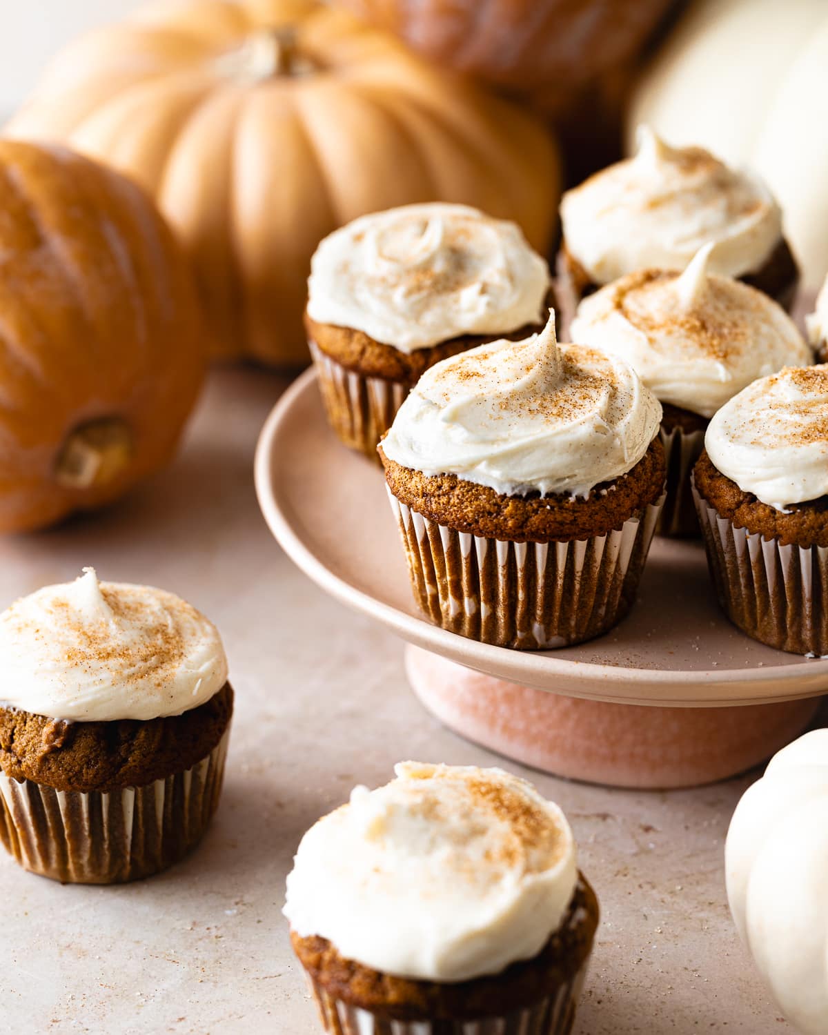 pumpkin cupcakes frosted and dusted with cinnamon sugar on a pink cake stand. 