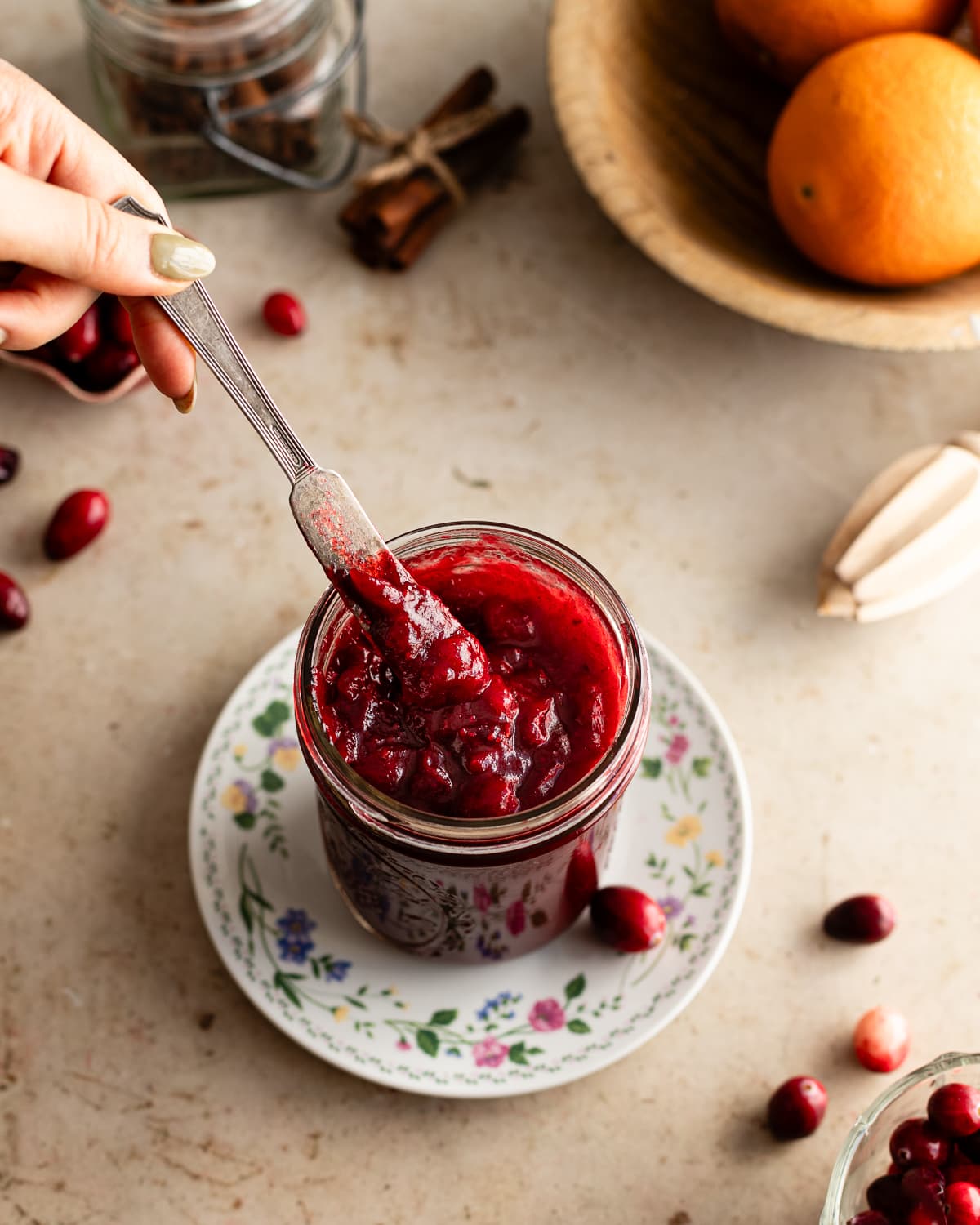 small spreader scooping cranberry jam out of jar on a small saucer. 