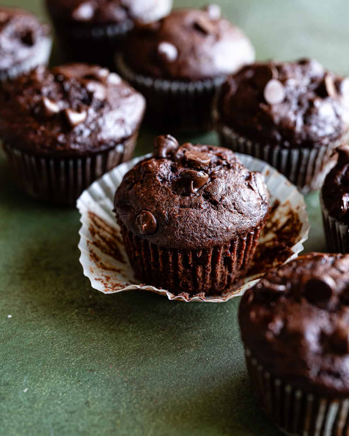 Chocolate zucchini muffins in a line with one of the wrappers unwrapped. 