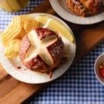 Pretzel bun on saucer with potato chips.