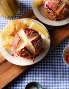 Pretzel bun on saucer with potato chips.