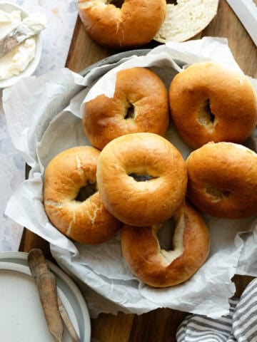 Bagels stacked in a pan lined with parchment paper.